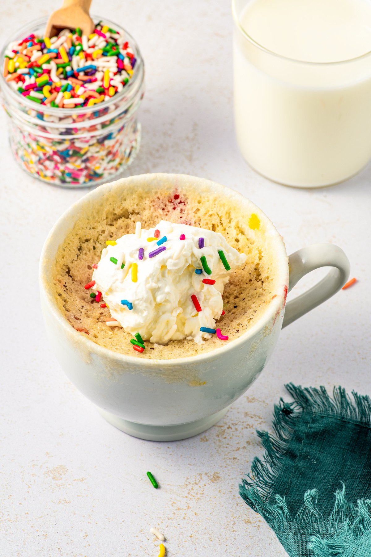 A cake in a mug, topped with whipped cream and sprinkles.
