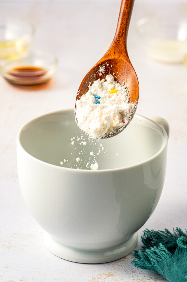 Sprinkling funfetti cake mix into a white mug.