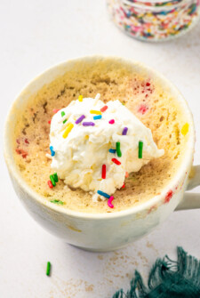 Vanilla cake in a cup, topped with sprinkles and a dollop of whipped cream.