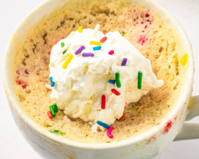 Vanilla cake in a cup, topped with sprinkles and a dollop of whipped cream.