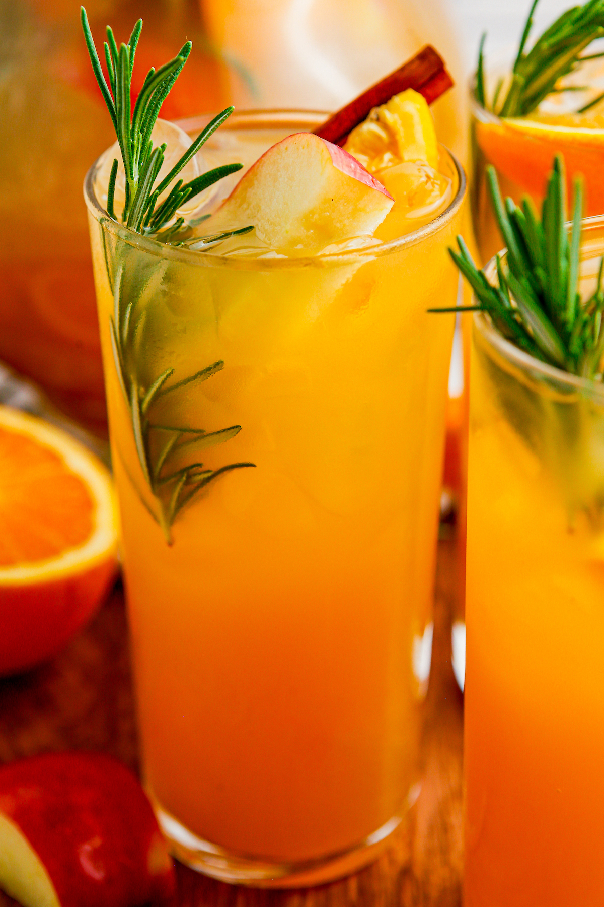 Tall glasses of apple cider punch with sprigs of rosemary and slices of apple.