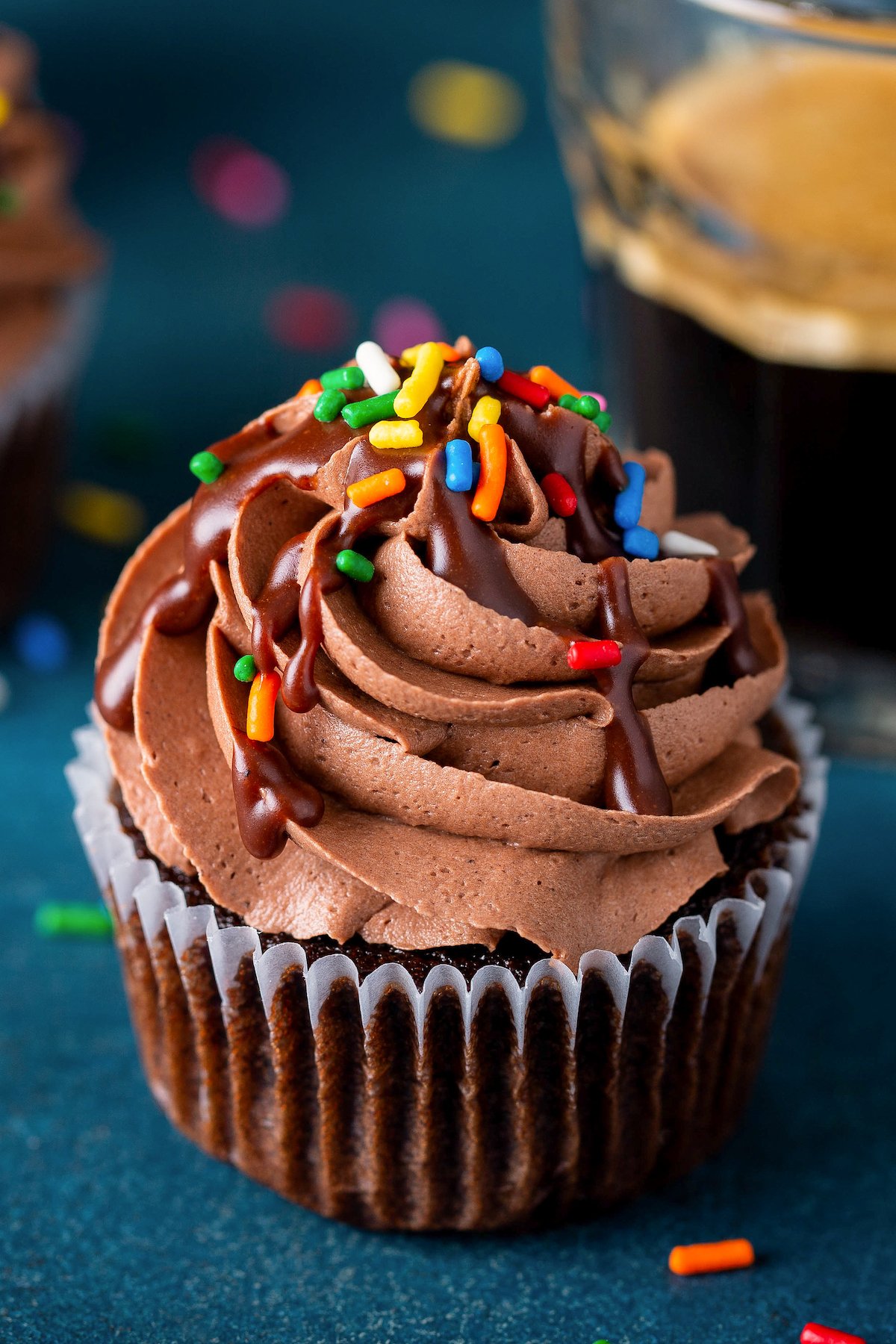 A chocolate cupcake with chocolate frosting and rainbow sprinkles.