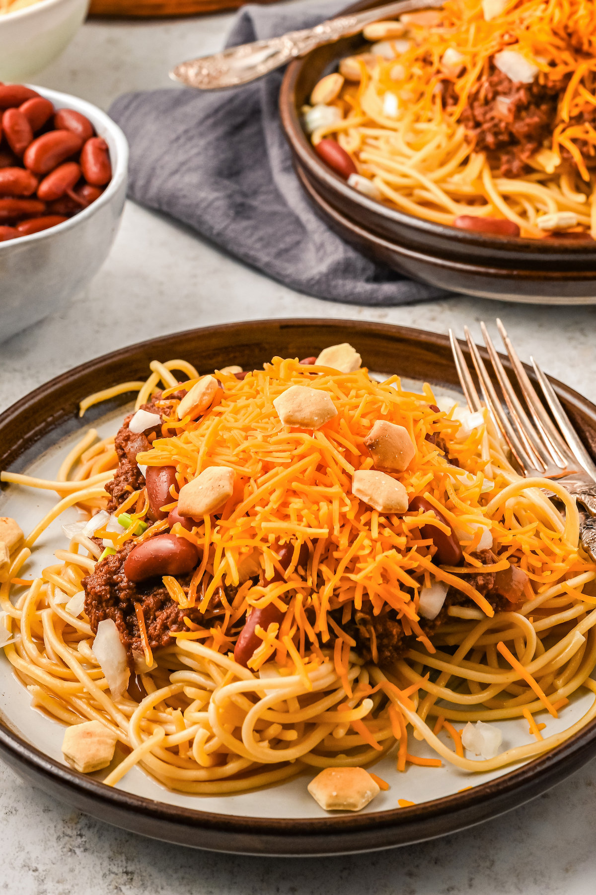 Chili and pasta on dinner plates, with shredded cheddar and other toppings.