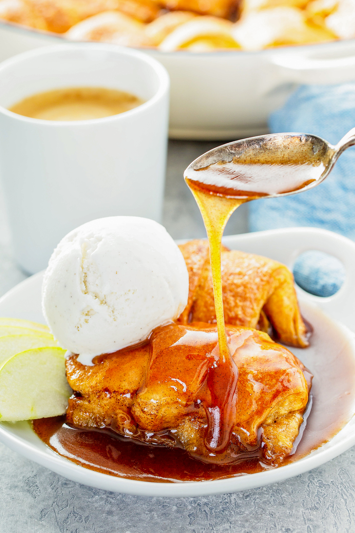 Sauce being drizzled over the top of an easy apple dumpling in a bowl with ice cream.