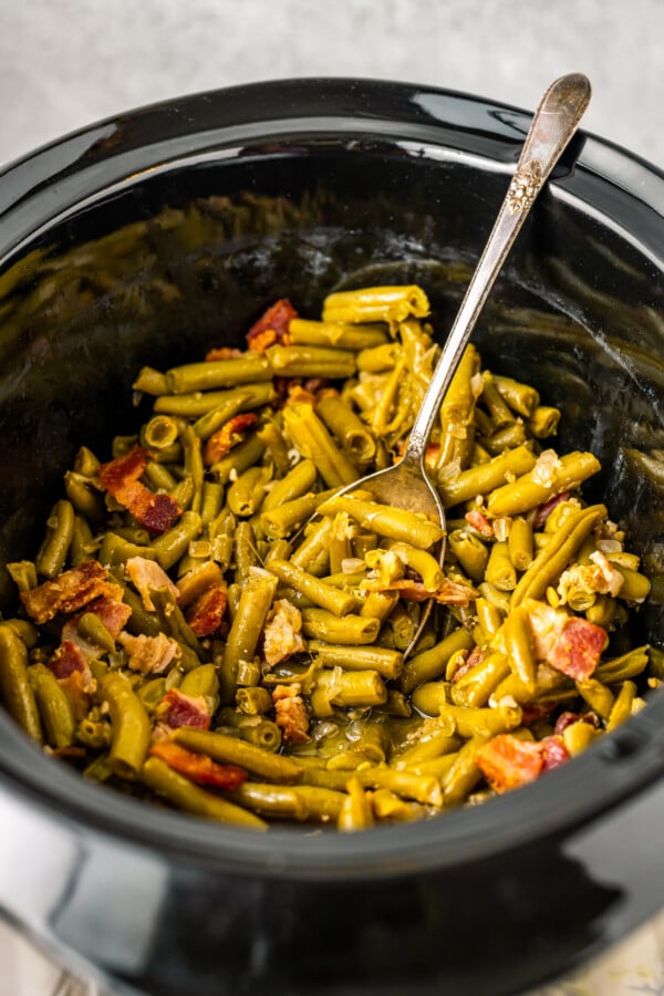 A spoon resting in a slow cooker full of green beans.