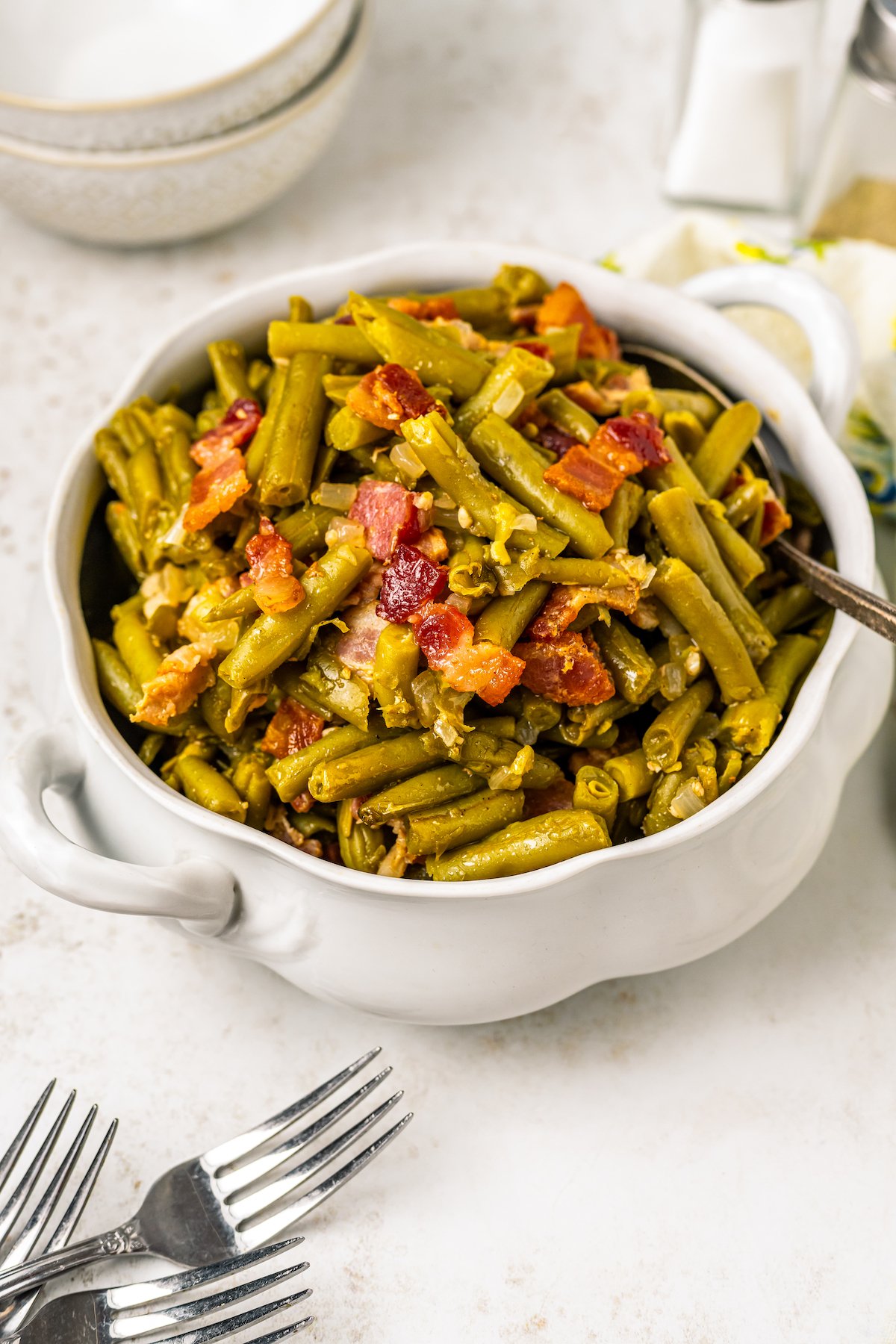 A two-handled serving bowl of green beans with bacon.