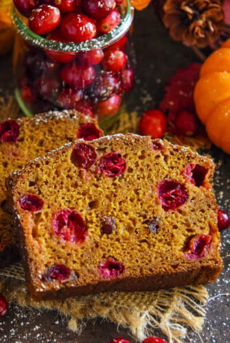 A slice of cranberry pumpkin bread stacked against a second slice of bread.