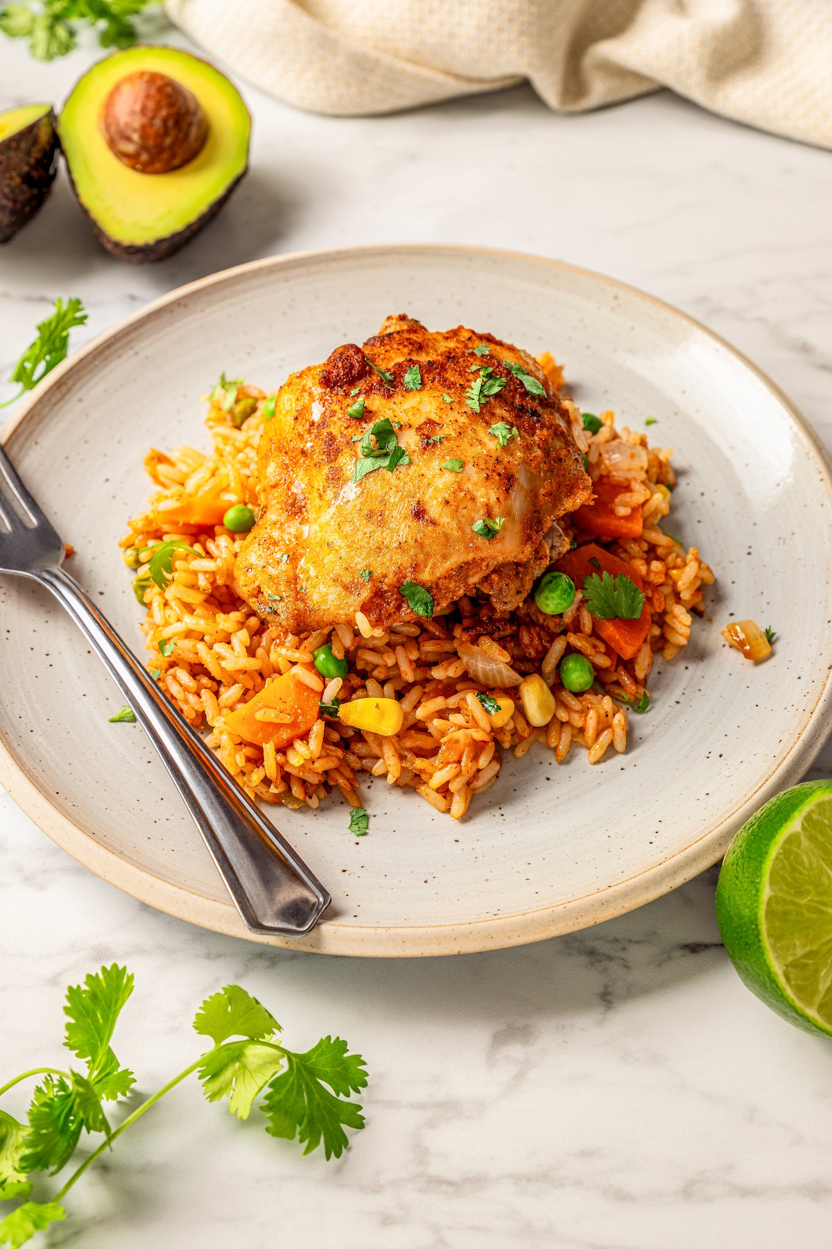 A plate filled with Mexican chicken and rice with fresh cilantro on top and a fork on the side of the plate.