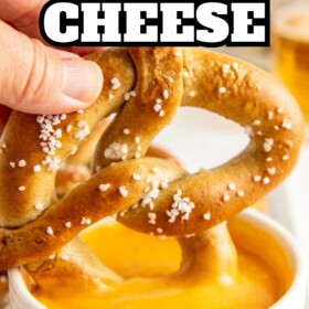 A soft pretzel being dunked in a bowl of beer cheese dip.