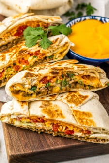 A Crunchwrap Supreme is golden, melty, and crunchy, sliced near a bowl of queso dip.