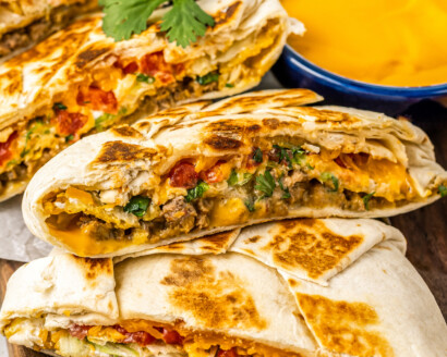 A Crunchwrap Supreme is golden, melty, and crunchy, sliced near a bowl of queso dip.