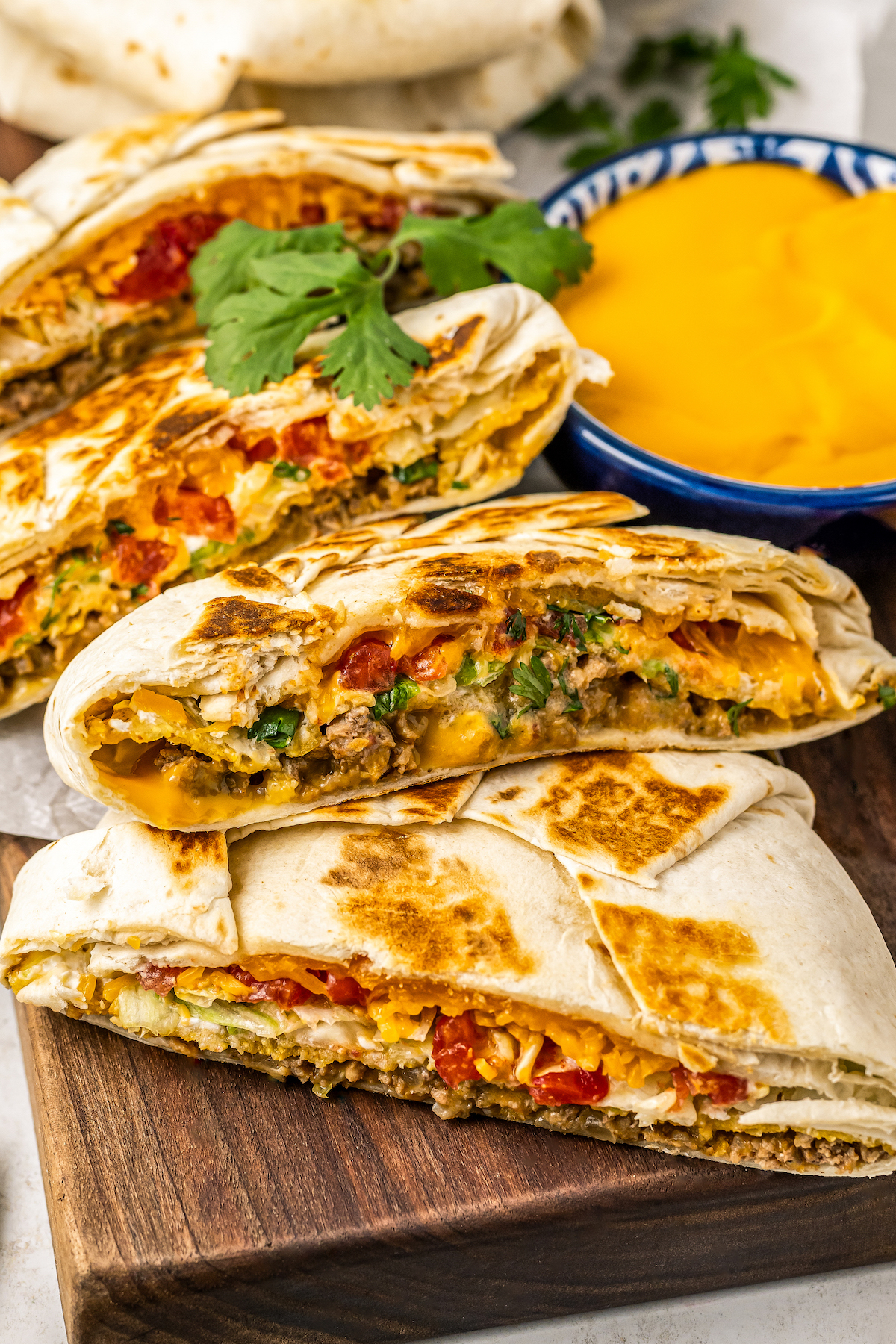 A Crunchwrap Supreme is sliced to show the inside near a bowl of queso dip.