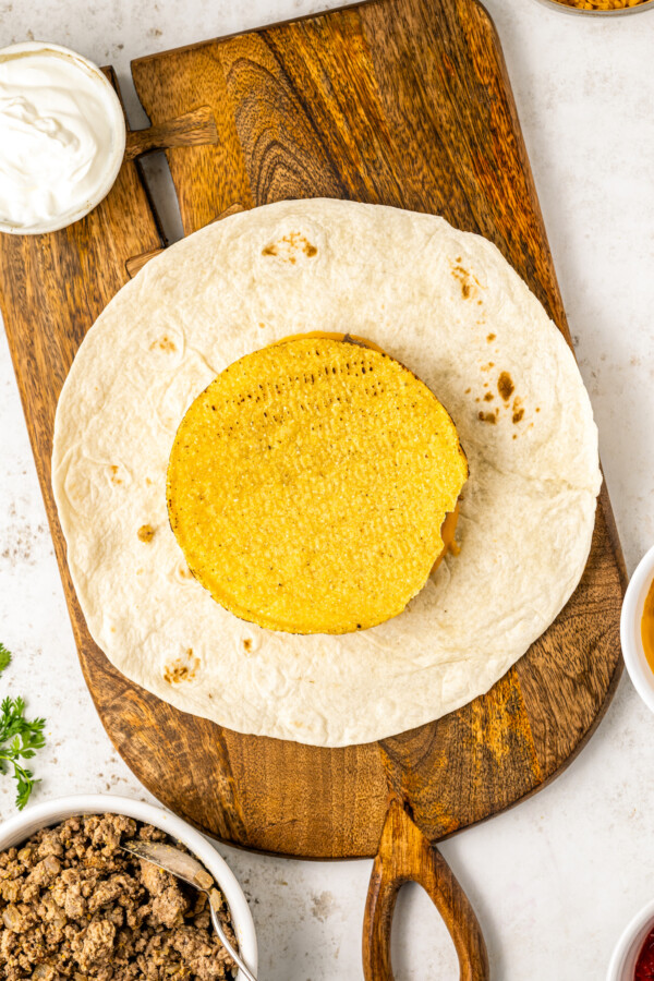 A crunchy corn tortilla is layered with beef and cheese on a soft tortilla.