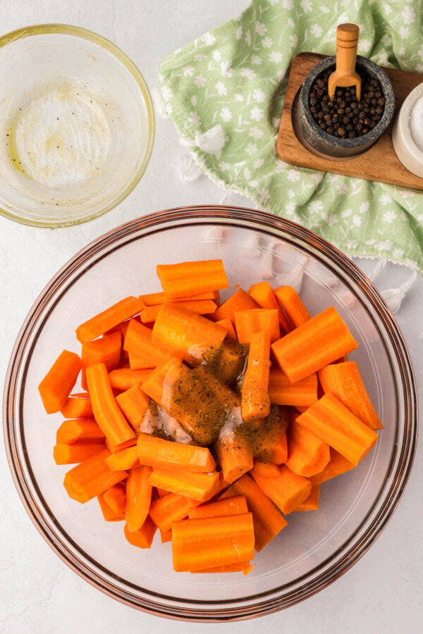 Raw carrots are cut in a bowl with honey, spices, and olive oil