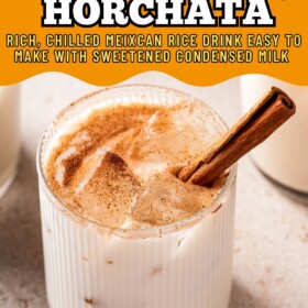 A glass of horchata with cinnamon on top and a cinnamon stick garnish.