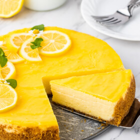A slice of lemon cheesecake is being cut and removed from the whole cheesecake.