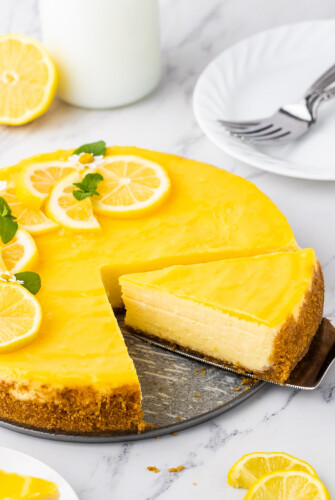 A slice of lemon cheesecake is being cut and removed from the whole cheesecake.