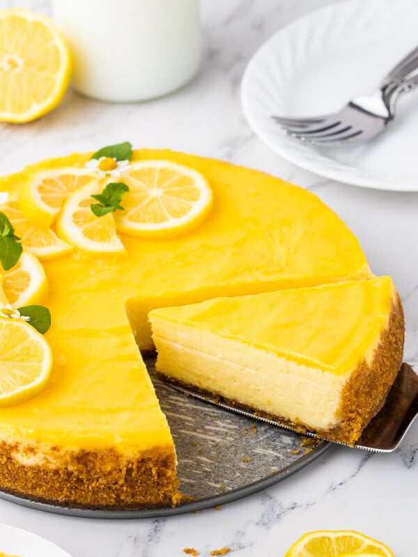 A slice of lemon cheesecake is being cut and removed from the whole cheesecake.