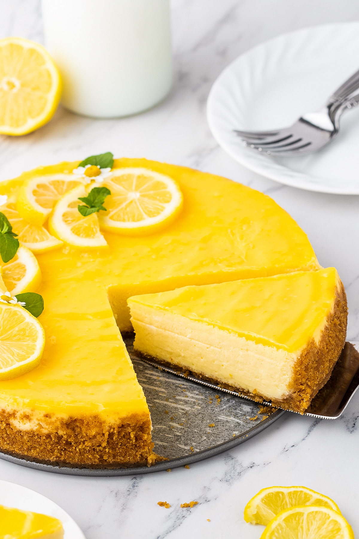 A slice of lemon cheesecake is being cut and removed from the whole cheesecake.