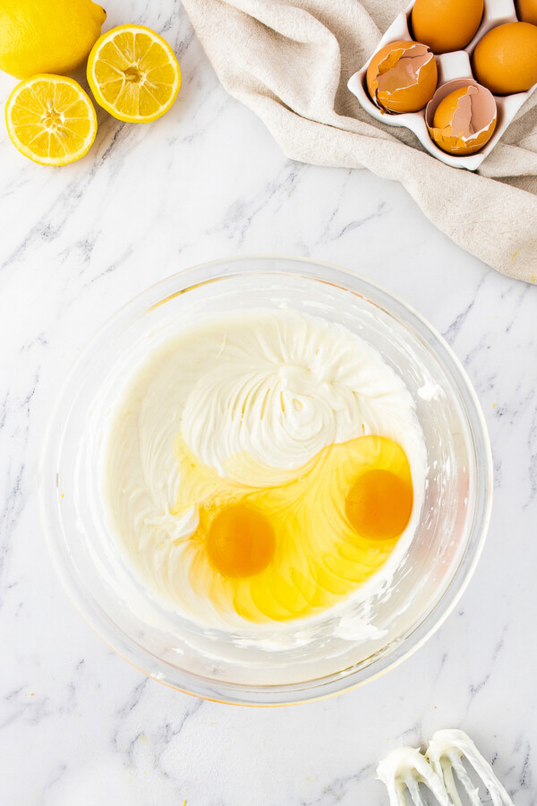 Two cracked eggs are in a bowl of whipped cream cheese