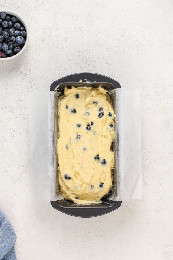 Lime Blueberry Pound Cake batter is in a loaf pan, lined with parchment paper.