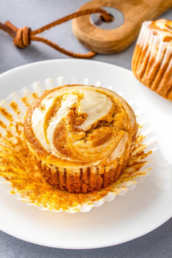 A pumpkin cream cheese muffin on a plate with the liner being pulled off.