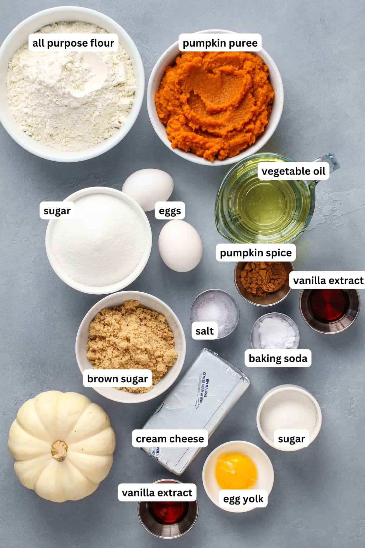 Ingredients for pumpkin cream cheese muffin recipe in bowls in order from top to bottom: all purpose flour, pumpkin puree, sugar, eggs, vegetable oil, pumpkin spice, vanilla extract, salt, baking soda, brown sugar, cream cheese, egg yolk.