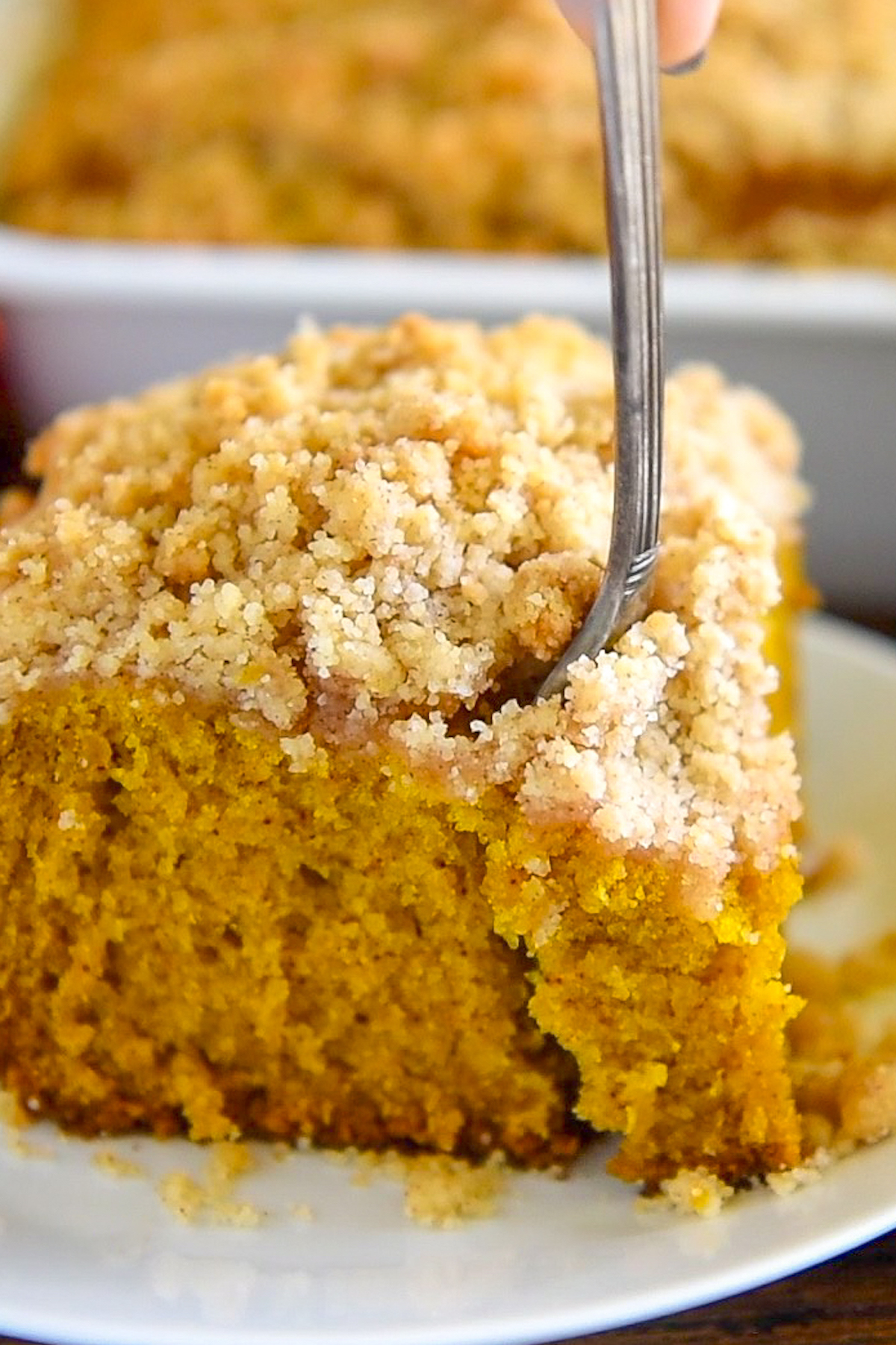 A slice of pumpkin coffee cake on a plate with a fork taking a bite.