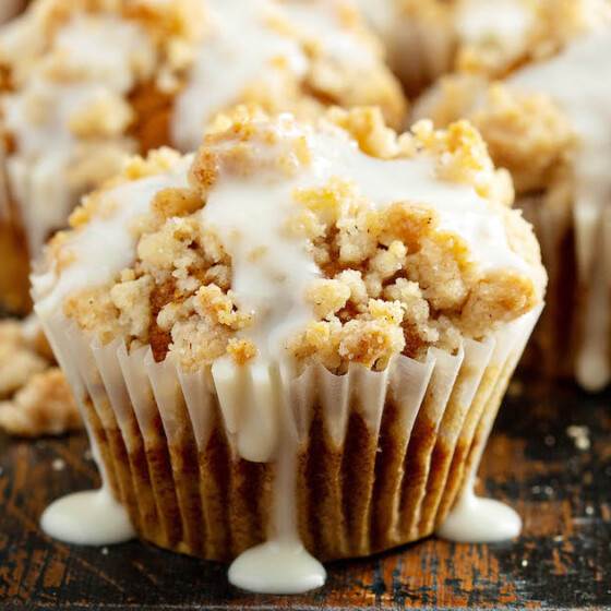 Pumpkin streusel muffins on a cutting board drizzled with cream cheese icing.