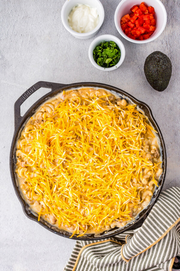 Shredded cheese added overtop of taco mac in a skillet.