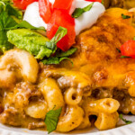 Close up of taco mac and cheese on a plate, garnished with diced tomatoes, avocado, and sour cream.