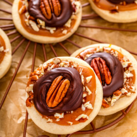 Turtle cookies with chocolate, caramel. and pecans cool on a rack.
