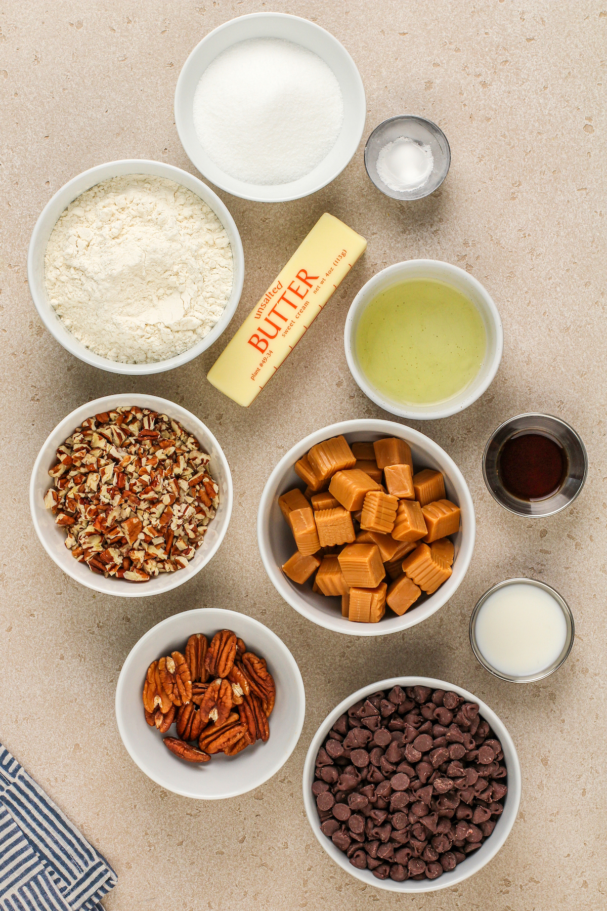 Ingredients to make turtle cookies are laid out in small bowls.