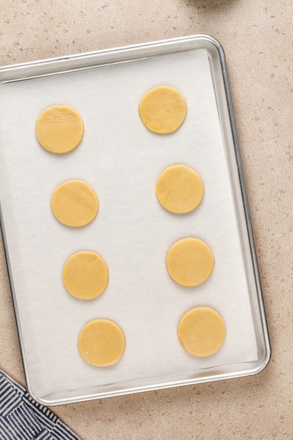 Sugar cookies sit on a baking sheet to be baked.