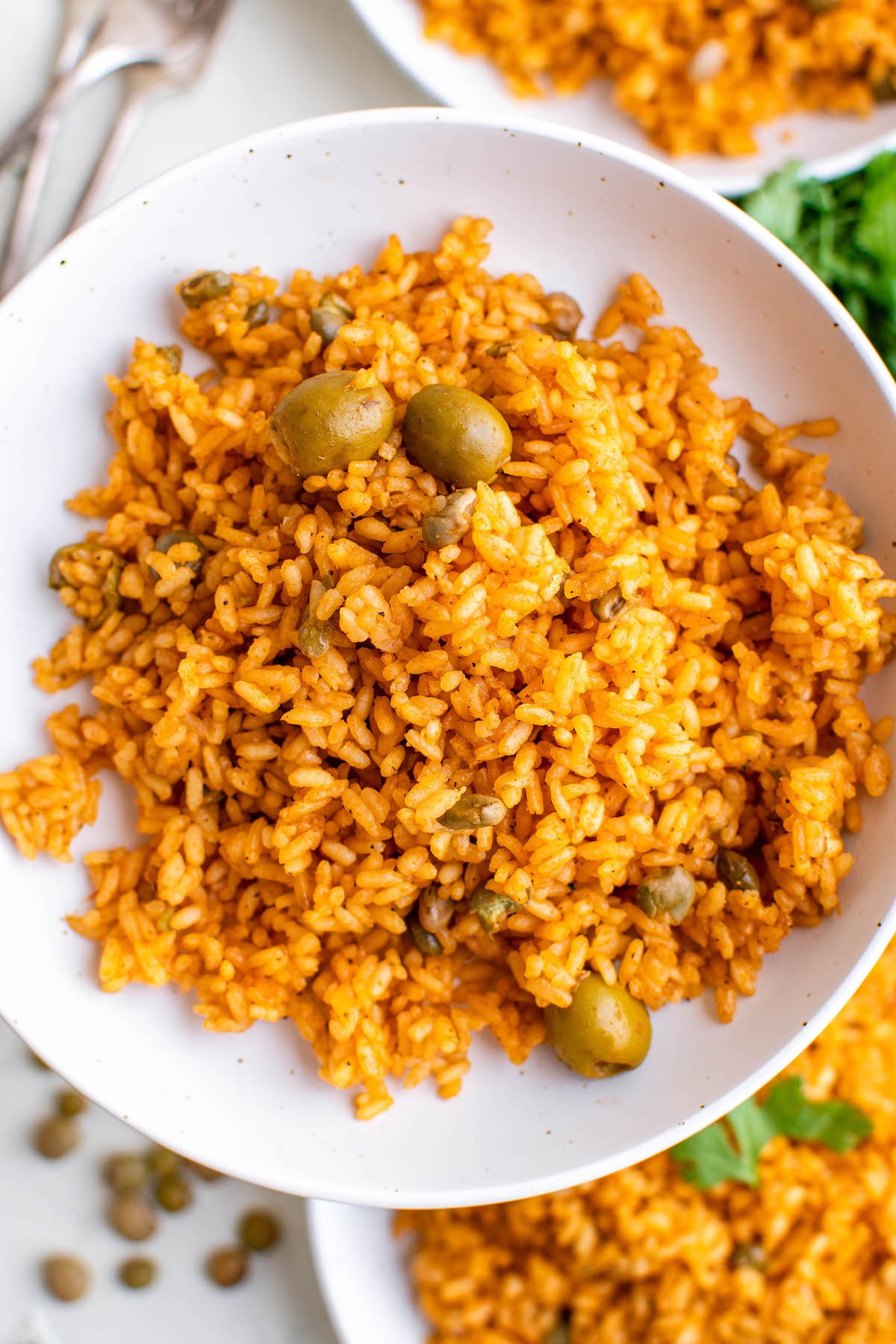 A while bowl filled with yellow arroz con gandules with whole olives.
