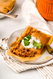 A homemade beef tamale unwrapped form the corn husk on a plate with a bite taken out to show the juicy shredded beef filling.