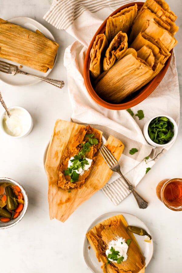 Beef tamales in a serving bowl and an unwrapped tamale on a plate topped with crema and cilantro. 