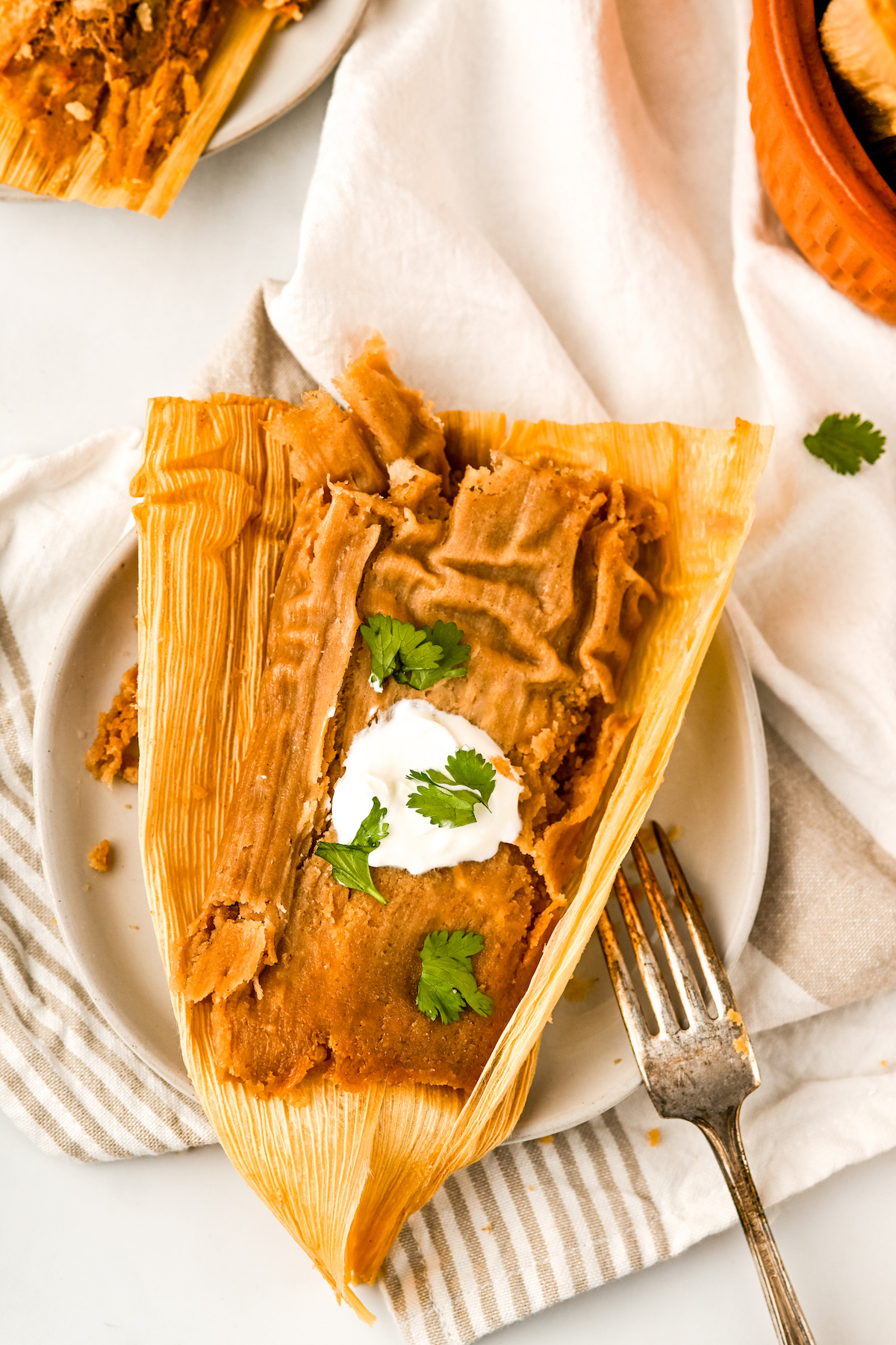 Open tamal in the husk with crema and cilantro.