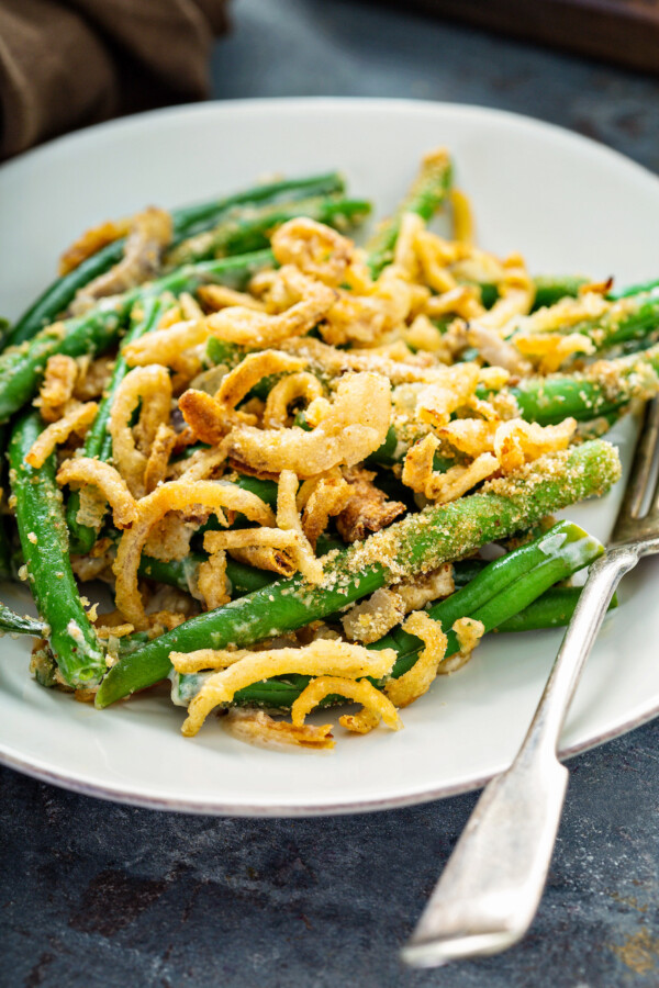 An up close image of a serving of the best green bean casserole with crispy fried onions and bread crumbs on a plate with a fork.