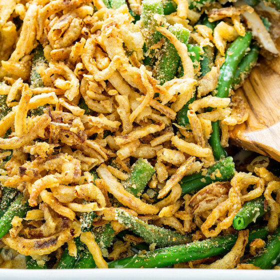 Green Bean Casserole with fresh green beans and crispy fried onions on top in a baking dish with a wooden spoon.