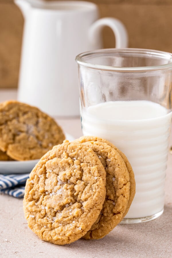Three chewy peanut butter cookies stacked against a glass of cold milk.