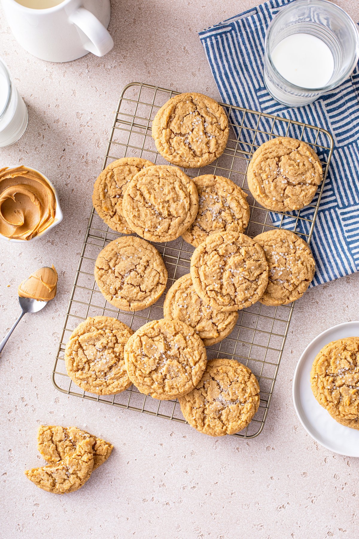 Peanut butter cookies with chewy centers and crisp edges arranged on a cooling rack with a spoonful of peanut butter and a glass of milk on the side.