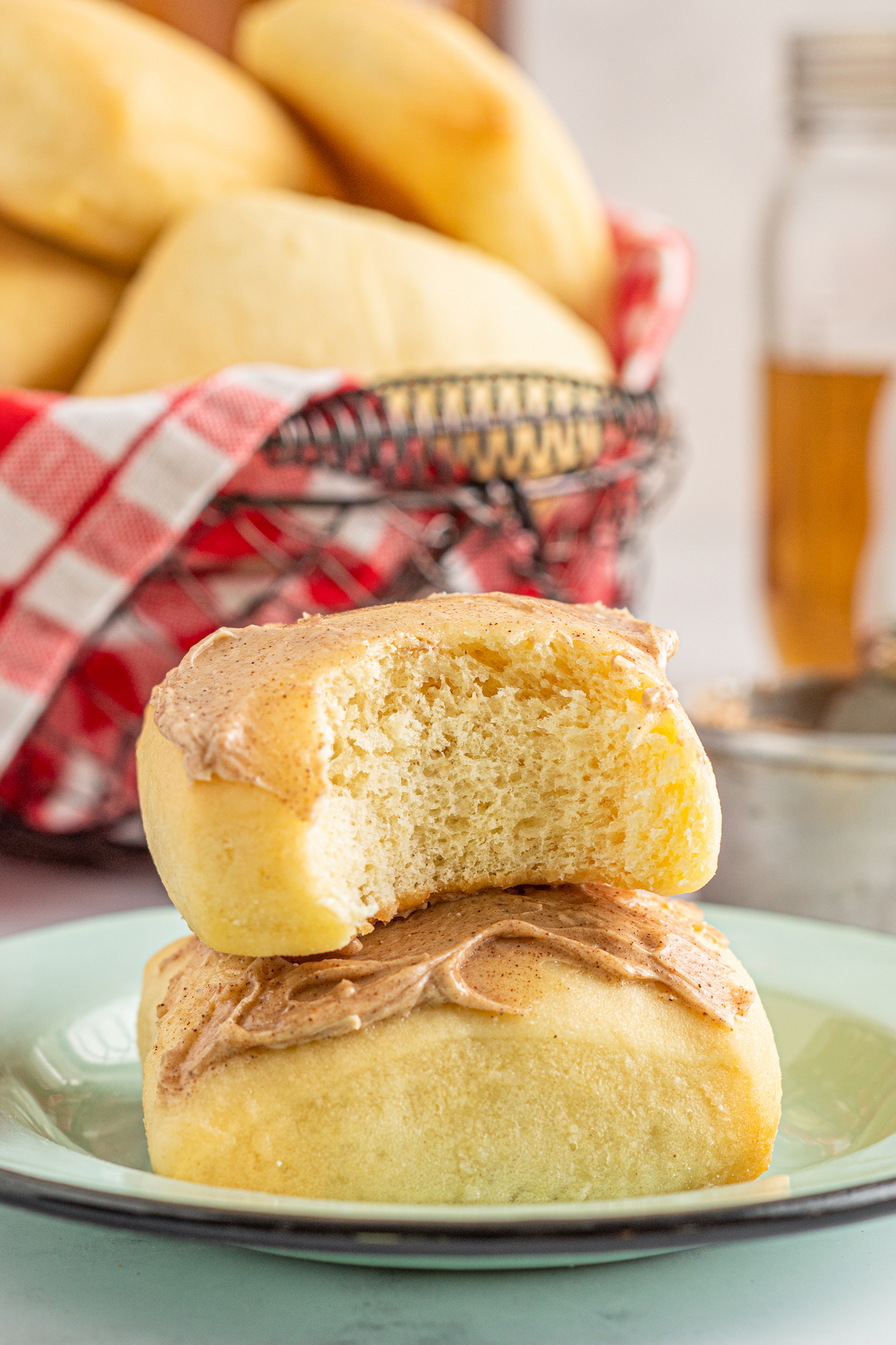 Two copycat Texas Roadhouse Rolls stacked on top of each other with cinnamon honey butter spread on top and a bite taken out of the top roll.