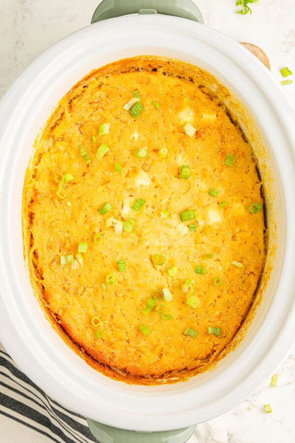 Cooked corn casserole with golden brown edges in the crockpot topped with sliced green onions.