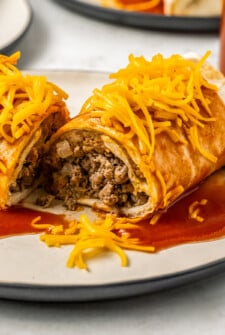 An Enchirito topped with Taco Bell hot sauce and shredded cheddar cheese that has been sliced in half to show the beef and bean filling.
