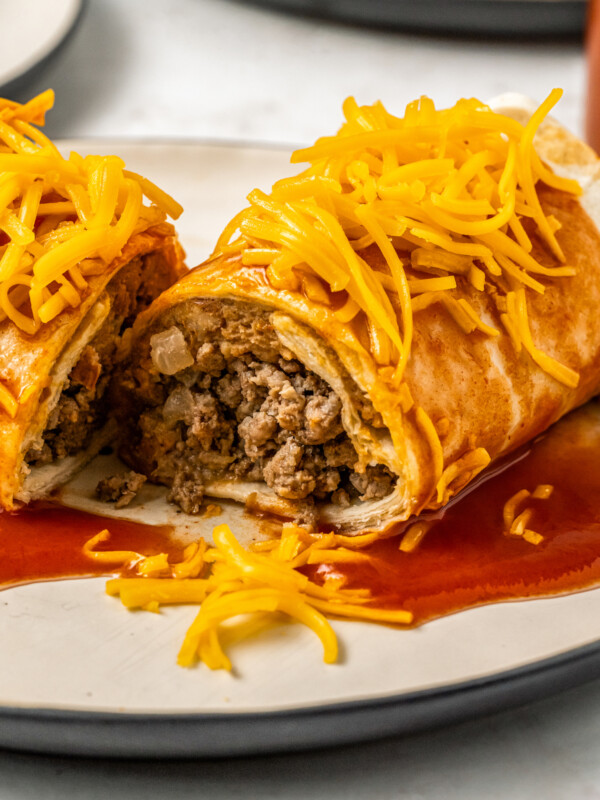An Enchirito topped with Taco Bell hot sauce and shredded cheddar cheese that has been sliced in half to show the beef and bean filling.