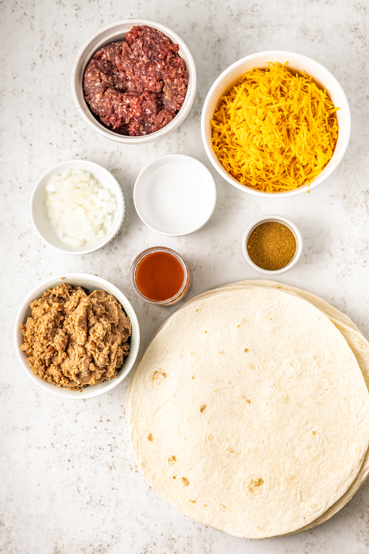 Ingredients needed for a Taco Bell enchirito recipe arranged in bowls on a countertop.