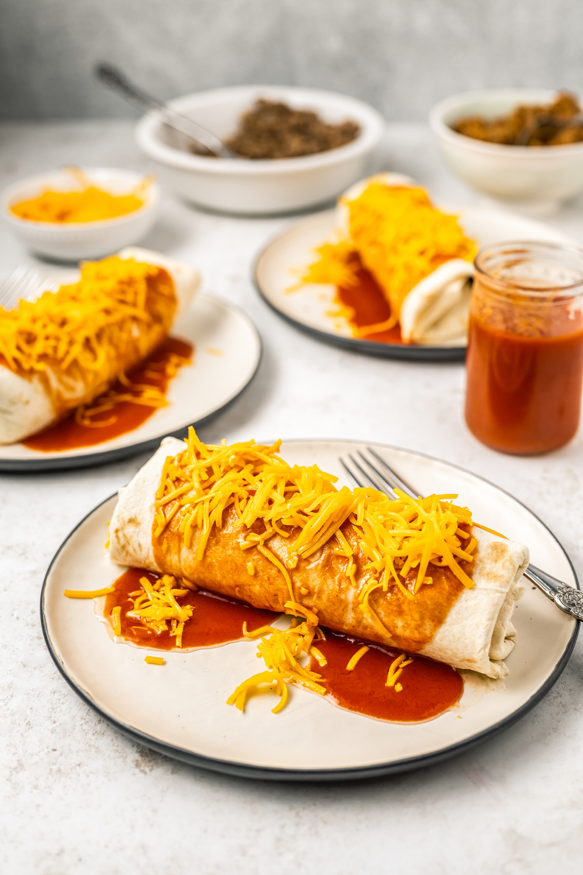 Three Taco Bell enchiritos on plates topped with red sauce and shredded cheddar cheese.