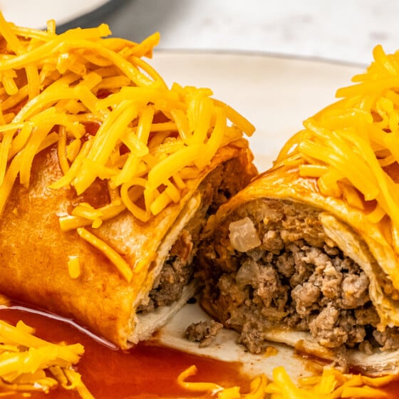 A Taco Bell Enchirito sliced in half to show the bean and meat filling and topped with red sauce and shredded cheddar cheese.