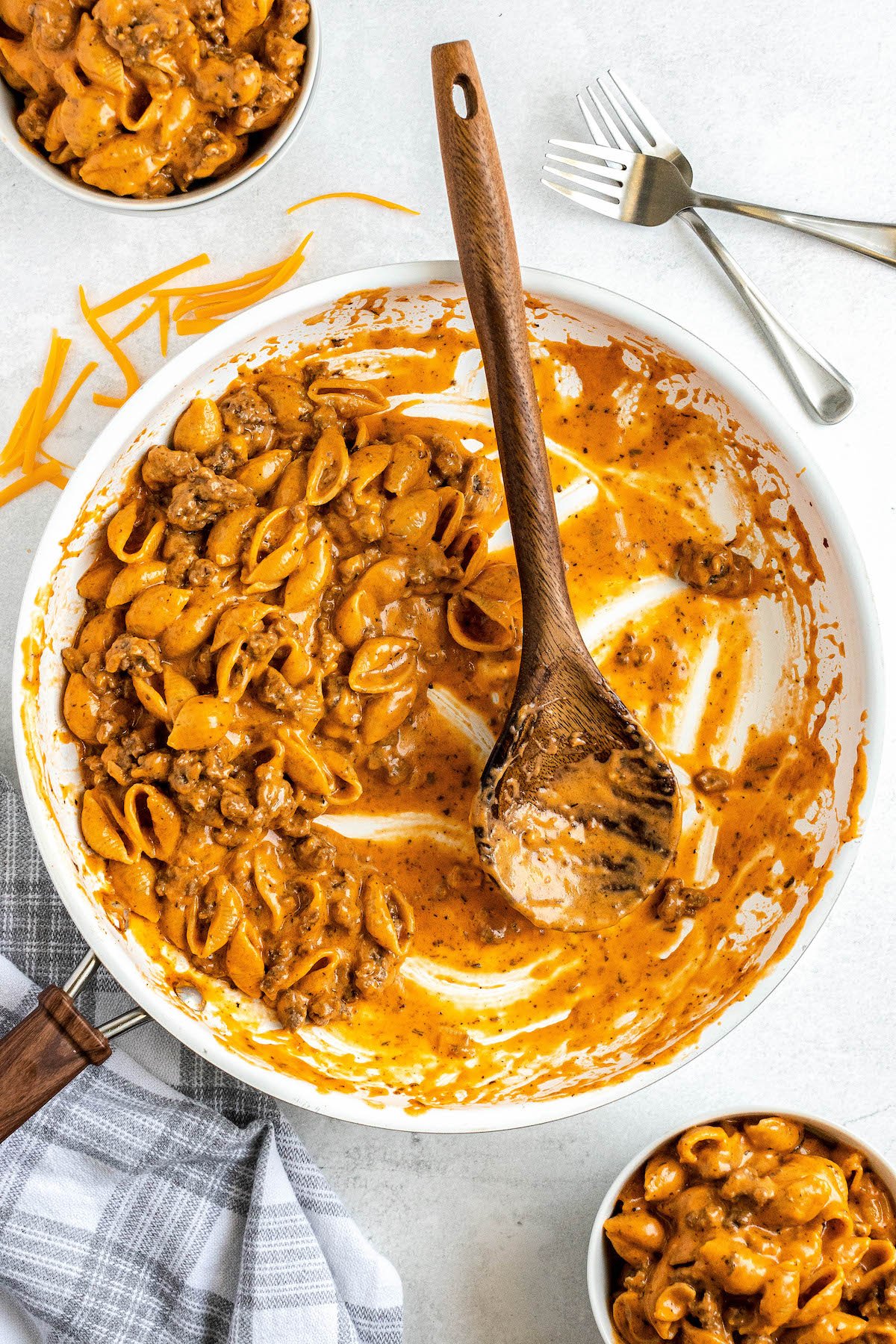 Homemade hamburger helper in a skillet with a wooden spoon adding servings to two bowls.